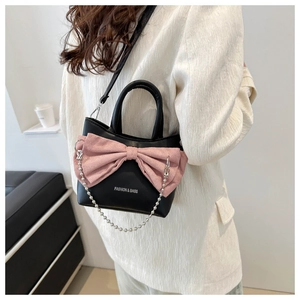 Detail of a black PU handbag featuring a pink bow, silver bead chain, and shoulder strap