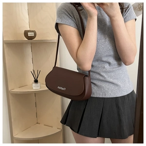 Close-up of a deep brown leather saddle bag featuring a fashion slogan detail on a shelf
