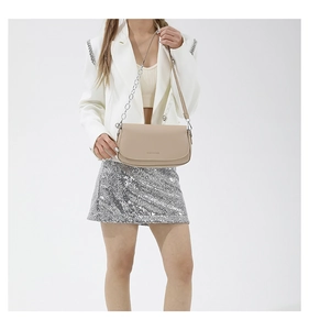 Detail of beige saddle bag with silver chain and leather strap on a model in a white blazer