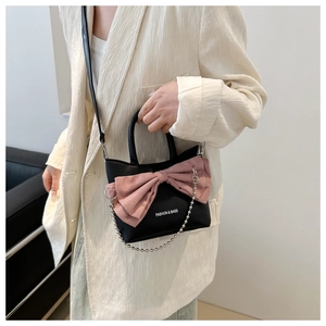 Détail du sac seau noir en cuir PU avec nœud rose, chaîne argentée et logo imprimé