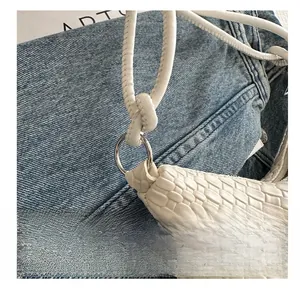 Close-up of white woven leather tote bag with silver metal ring and strap on denim background