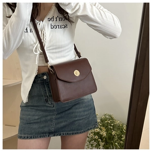 Détail d'un petit sac bandoulière marron foncé avec boucle dorée ronde en relief