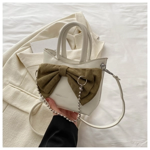 Close-up of cream bucket bag featuring a green suede bow and silver bead chain