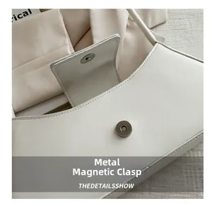 Dettaglio della chiusura magnetica in metallo argento su una borsa a tracolla bianca minimale