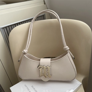 Minimalist beige moon bag with gold logo and knotted straps on a chair