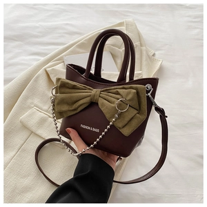 Close-up of contrast bow detail and silver chain on dark brown PU leather bucket bag
