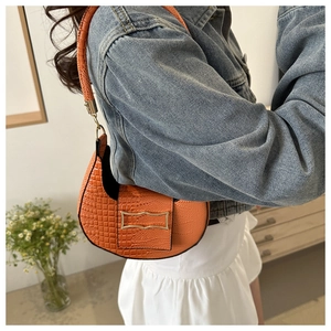 Detail of bright orange crescent bag with crocodile texture and gold metal clasp