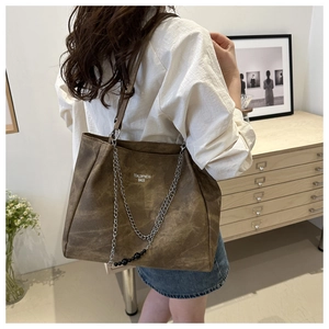 Detail of brown tote bag with silver chain and beaded charm in a lifestyle setting