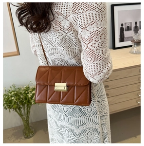 Rear view of model wearing a brown quilted crossbody bag with gold lock and chain strap