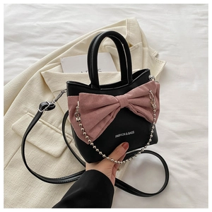 Detail of black leather bucket bag featuring a large pink bow and silver chain strap