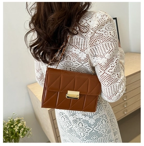 Brown quilted crossbody bag with gold chain strap worn with white lace dress in a room