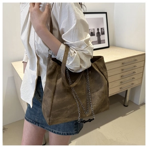 Close-up of a large dark brown tote bag with metal chain detail on a model's shoulder