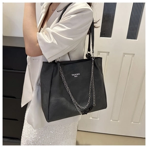Detail of black tote bag featuring chain straps and white text on matte leather