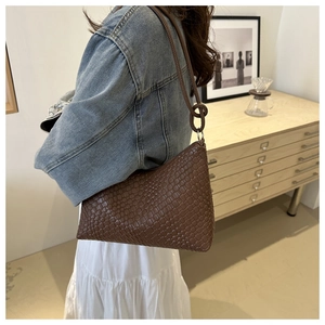 Close-up of brown woven shoulder bag featuring a unique knotted strap and sleek zipper
