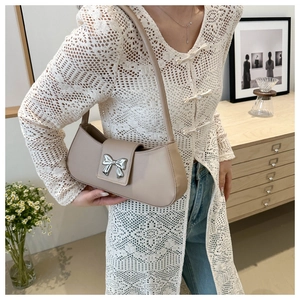 Detail view of beige shoulder bag with silver bow ornament worn with lace cardigan