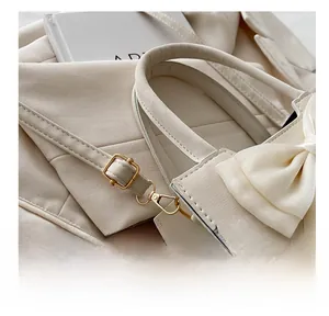 Detailed close-up of cream white leather handbag with bow and golden hardware