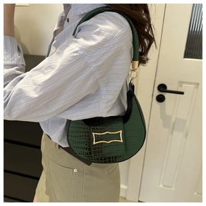 Close-up of dark green embossed leather shoulder bag with gold clasp and crocodile texture