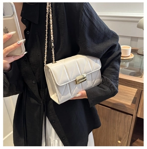 Detail view of a white quilted crossbody bag with a gold clasp held by a person