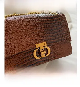 Dettaglio borsa marrone in pelle coccodrillo con chiusura a scatto dorata e tracolla a catena