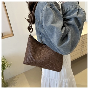 Detailed shot of brown woven leather shoulder bag with decorative knotted strap detail