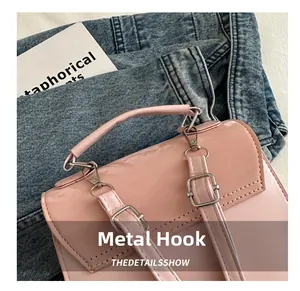 Close-up of pink glossy handbag featuring silver metal hooks and buckle strap details