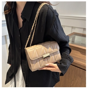 Detail view of a beige quilted crossbody bag with gold chain strap worn by a model
