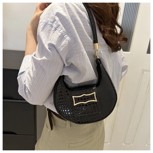 Detail of a black crocodile-embossed crescent hobo bag with a gold wavy buckle