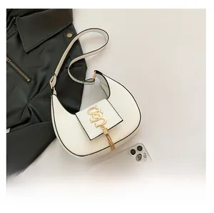 White crescent underarm bag with gold SS logo and tassel, showing size next to a phone