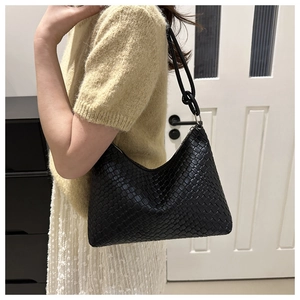 Side view of a black woven leather hobo shoulder bag worn by a model in a minimal setting