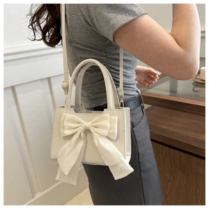 Close-up of a white crossbody bag featuring a large decorative bow and leather strap