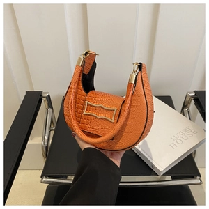 Detail of orange faux crocodile skin texture and gold buckle on a crescent handbag