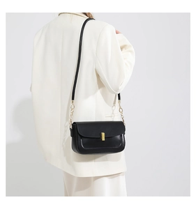 Minimalist black leather crossbody bag with gold lock shown on model in white blazer