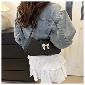 Dettaglio di una borsa a spalla nera con fibbia a fiocco argento indossata da modella