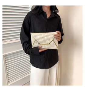 Detail of cream patent leather envelope clutch with embossed texture and gold metal trim