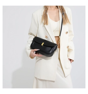 Detail of minimalist black leather crossbody bag featuring gold metal chain and buckle