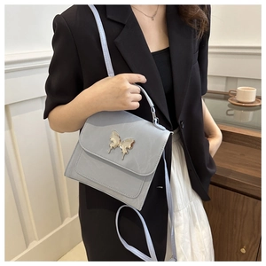 Close-up of light blue leather crossbody bag with a gold butterfly clasp worn on a black suit