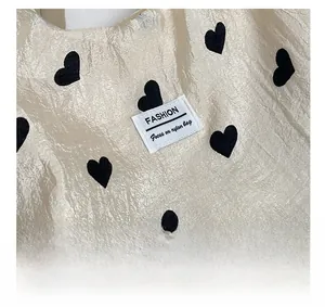 Close-up of beige nylon tote bag featuring black heart patterns and fashion logo detail
