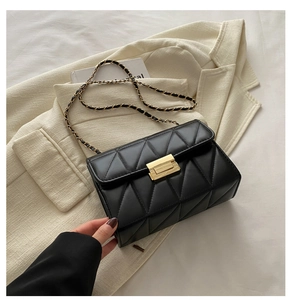 Detail of black quilted crossbody bag with gold metal clasp and woven chain strap