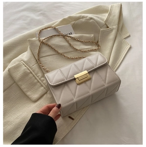 Detail of cream quilted crossbody bag with gold chain strap on a beige blazer background