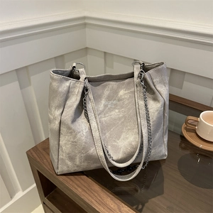 Grey vintage oversized tote bag with metal chain strap and logo in a cozy indoor setting