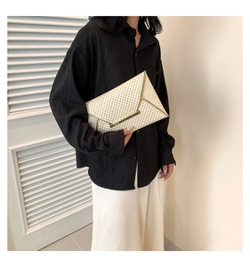 Detail of cream patent envelope clutch featuring gold metal trim and honeycomb texture
