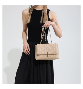 Close-up of beige quilted shoulder bag with gold chain and metal lock on model