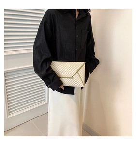 Close-up of beige patent leather clutch with diamond embossed texture and golden V-shaped trim
