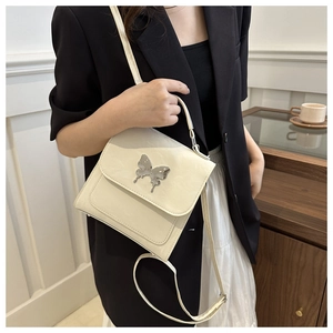 Detail view of a cream-colored handbag with a large silver butterfly metal buckle decoration
