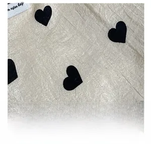 Macro shot of cream textured fabric with black heart prints and a small white brand label