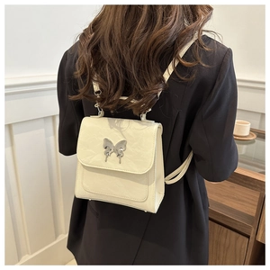 Close-up of cream white pleated leather bag with silver butterfly buckle on black blazer