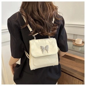 Détail du mini sac à dos blanc cassé avec boucle papillon argentée sur blazer noir