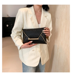 Detailed view of black patent leather envelope clutch with gold hardware held by a model