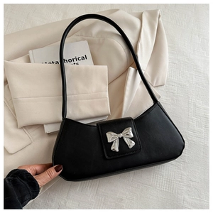 Detail of black underarm bag featuring a silver metal bow on polished faux leather