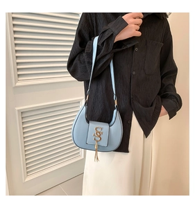 Detail of light blue crescent underarm bag with gold S logo and fringe on a model